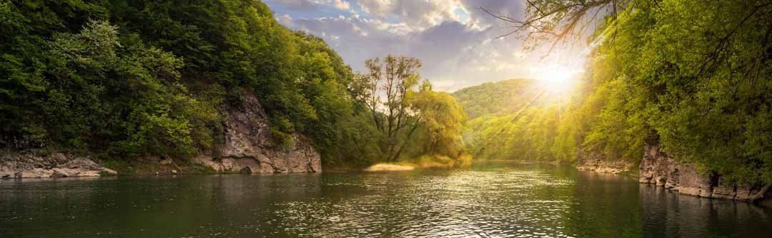 Forest river at sunset with stones along the shore, creating a tranquil and serene atmosphere.