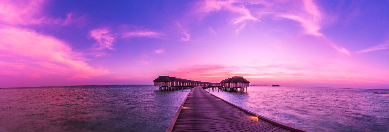 Maldives sunset panorama with villas, colorful sky, and sea, creating a tranquil, exotic scene.