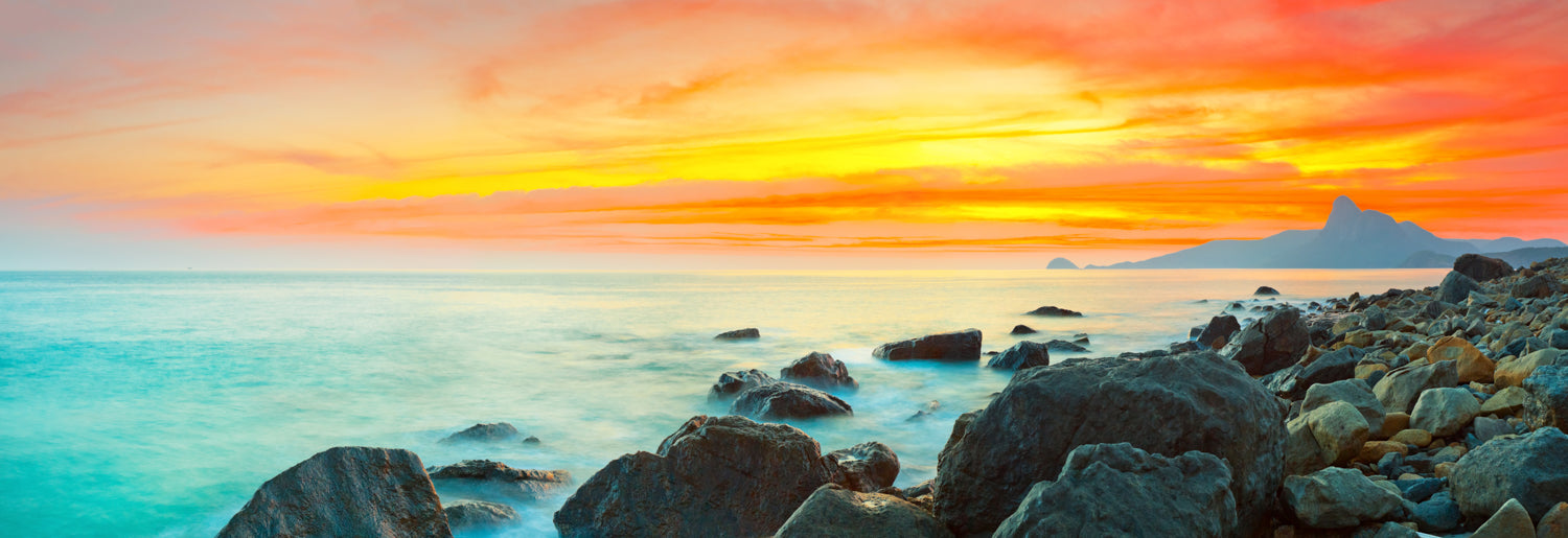 Panoramic sunset mural over sea with stone foreground, perfect for indoor and outdoor spaces.